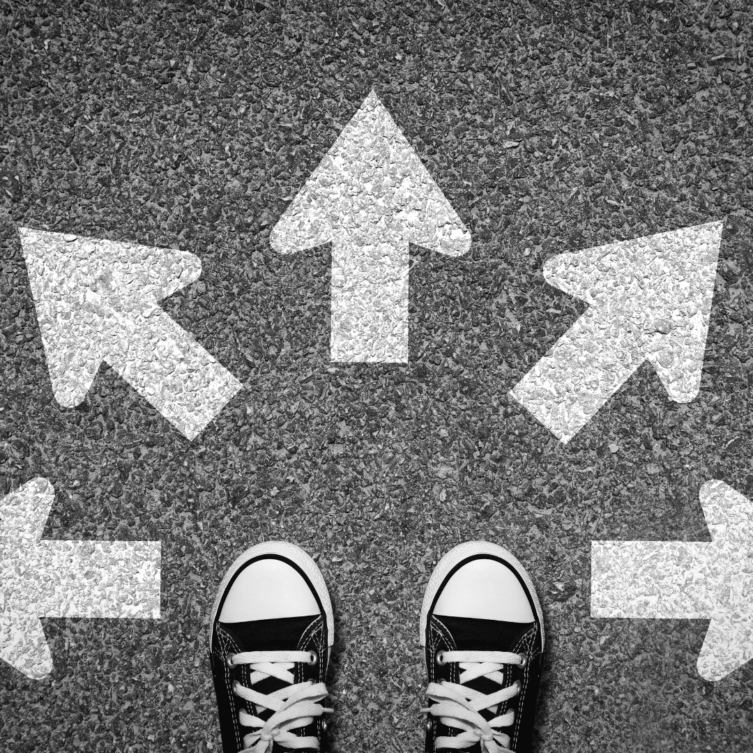 The image shows an asphalt background with five arrows pointing in different directions. A pair of converse sneakers are at the bottom of the image to illustrate someone coming to a choice point. This illustrates choices.